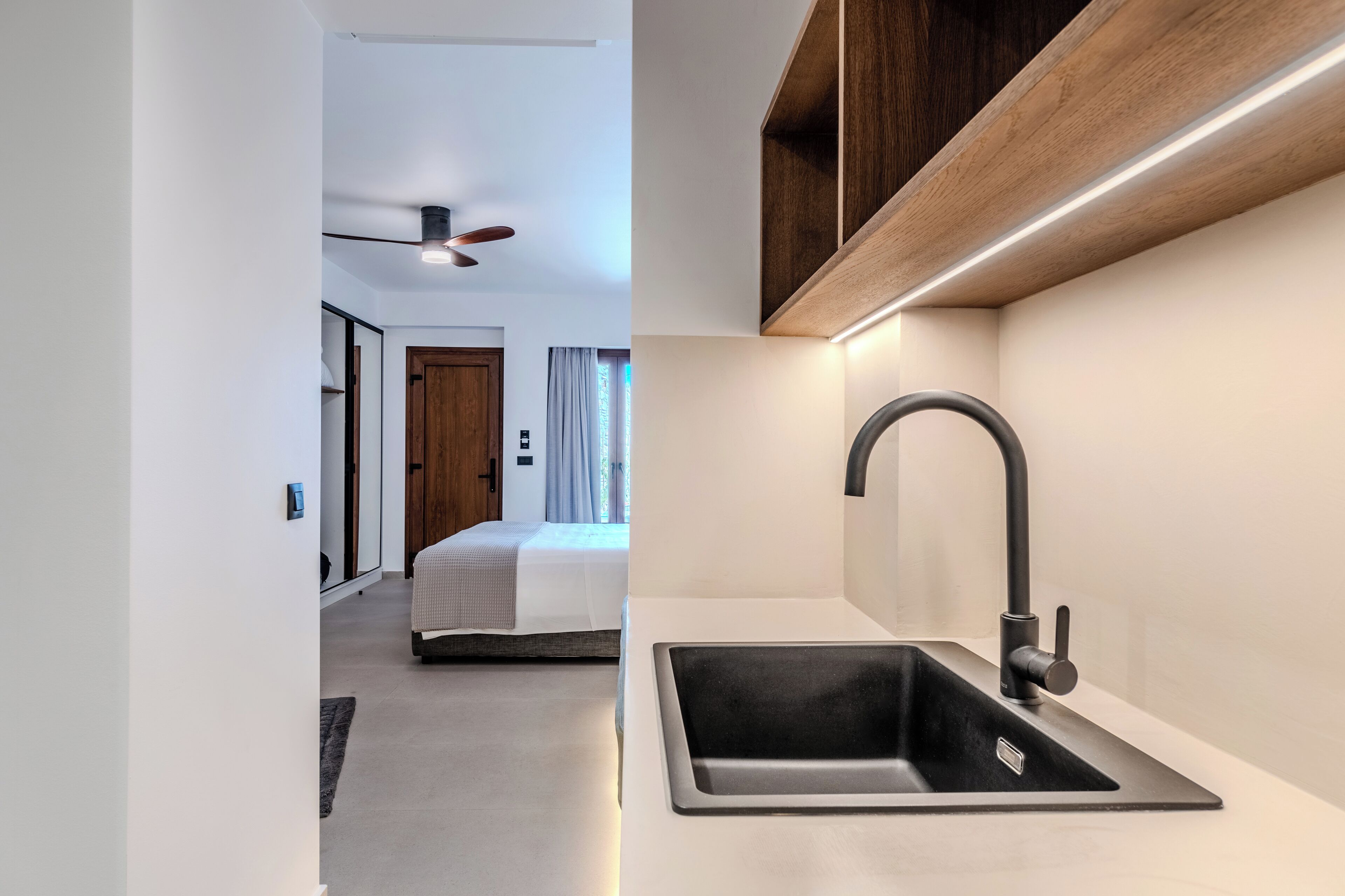 A modern hotel room with a large bed, a built-in sink, and a ceiling fan.