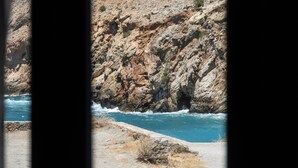 Un paisaje costero rocoso con vista despejada al mar a través de una ventana con barrotes.