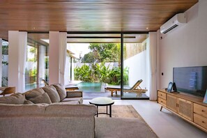 A modern living room with a large sofa, a TV, and a pool visible through glass doors. - Vihanna Canggu (Canggu)
