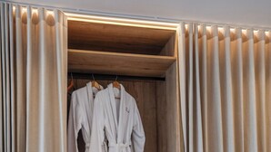 A hotel room with a wooden wardrobe, two white bathrobes hanging, and two folded towels on the bed. - Seaside 9: Modern Studio with Balcony & Ocean View (Cape Town)