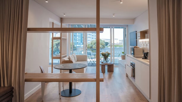 A modern hotel room with a large window, a dining area, and a kitchenette. - Seaside 9: Modern Studio with Balcony & Ocean View (Cape Town)