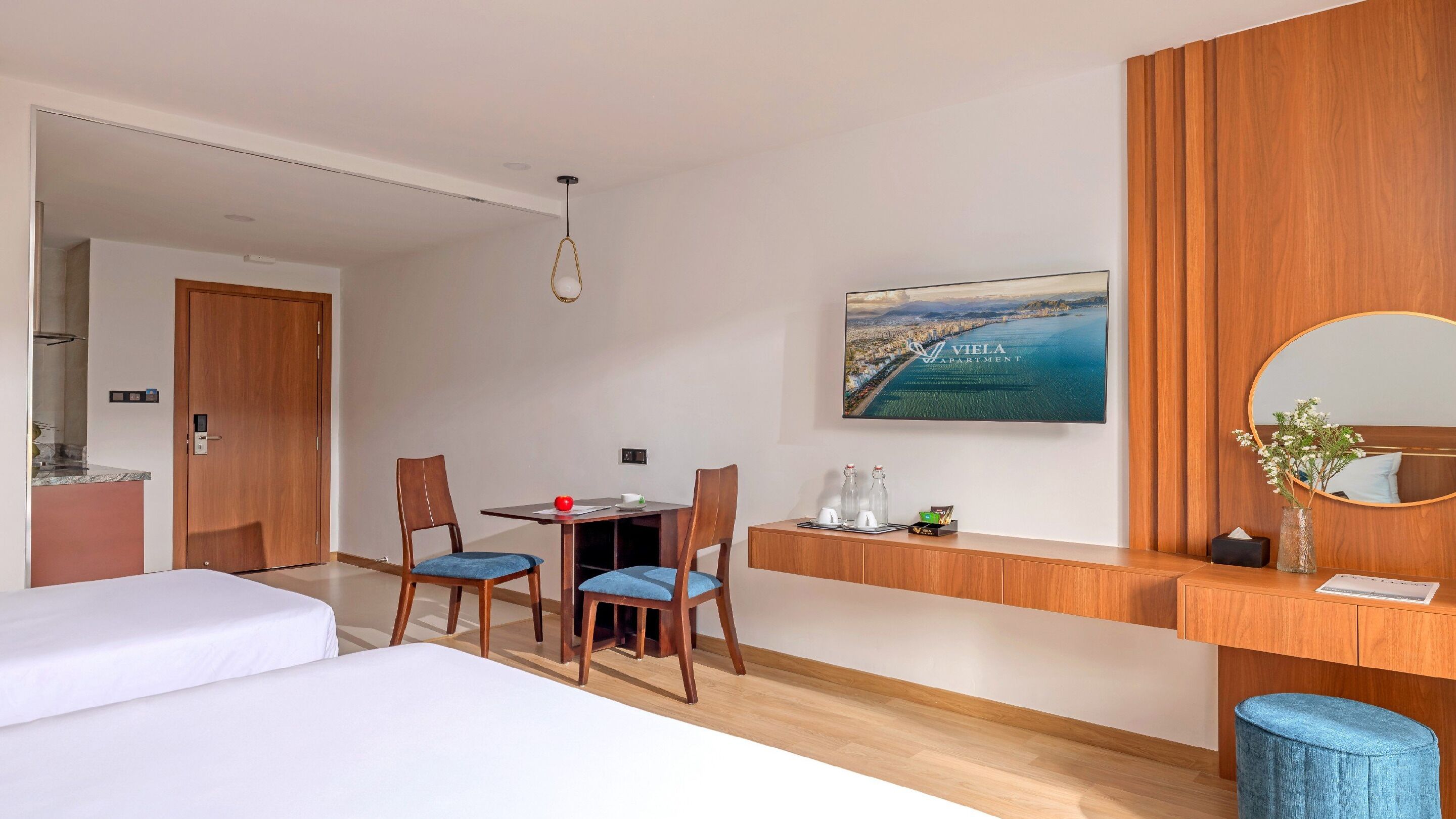 A hotel room with a bed, a desk with two chairs, a small table, a mirror, and a large window with a cityscape view.
