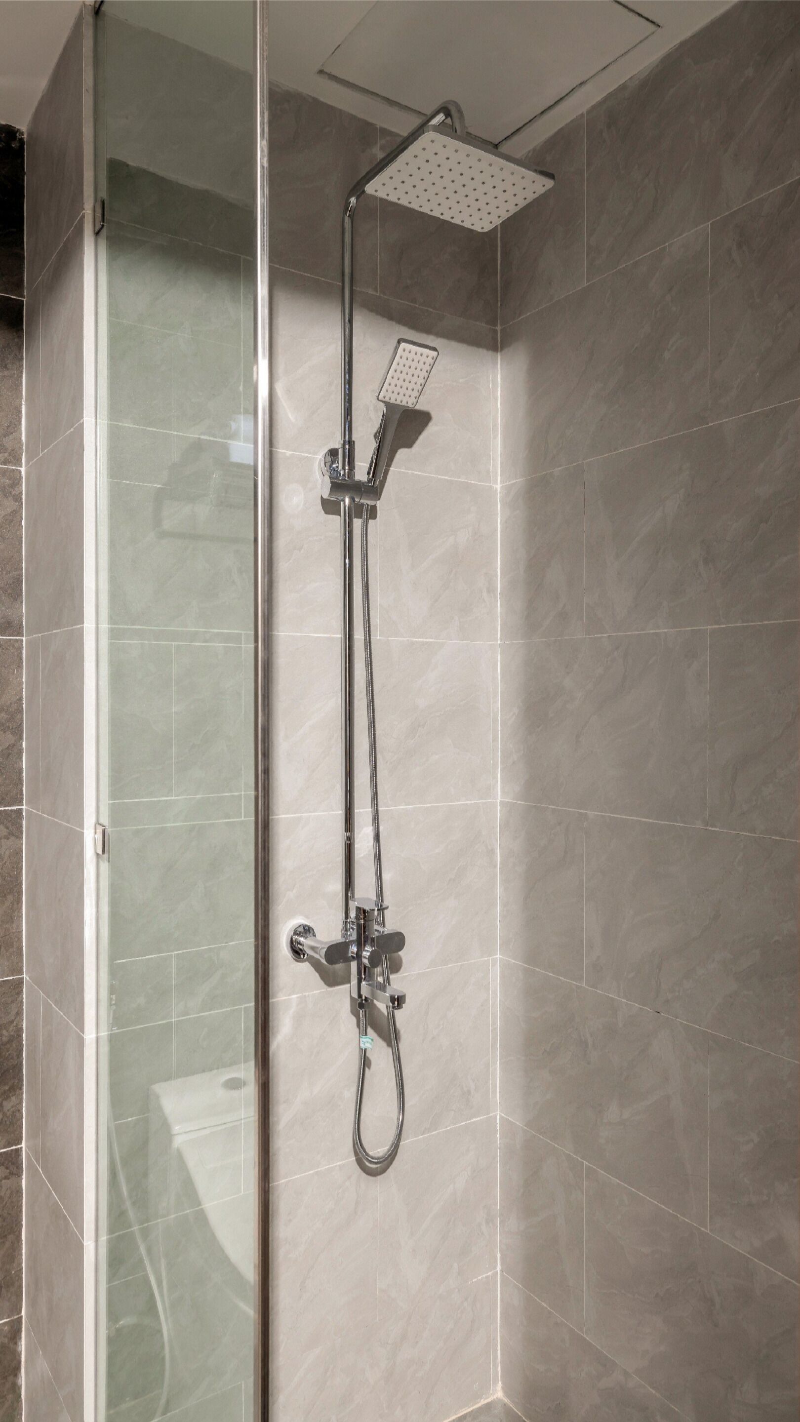 A shower with a handheld showerhead and a fixed showerhead, mounted on a wall with a tiled floor.