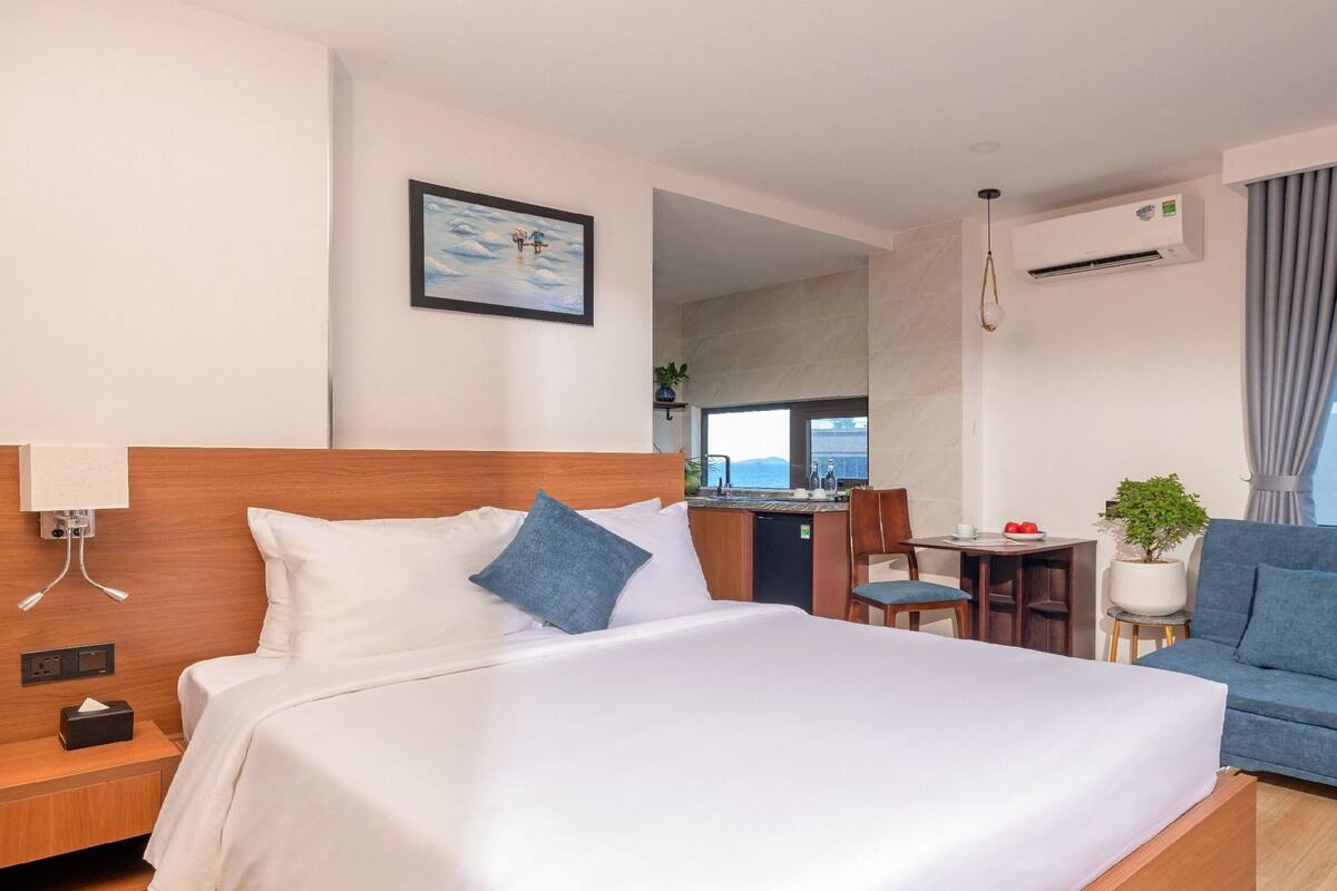 Habitación de hotel con una cama grande, un sofá, un escritorio con vistas y una pequeña planta en maceta.