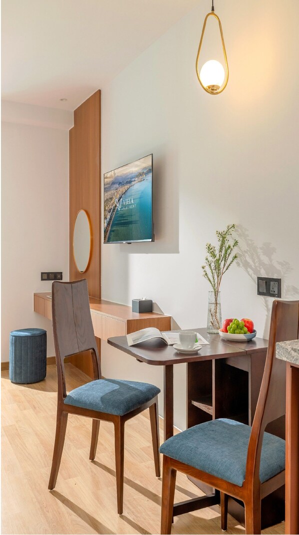 A modern dining area with wooden chairs and a table, a mounted television, and a vase with flowers. - Viela Apartment Nha Trang  (Nha Trang)