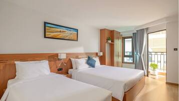 A hotel room with two beds, a painting on the wall, a window with curtains, and a view of the outside.