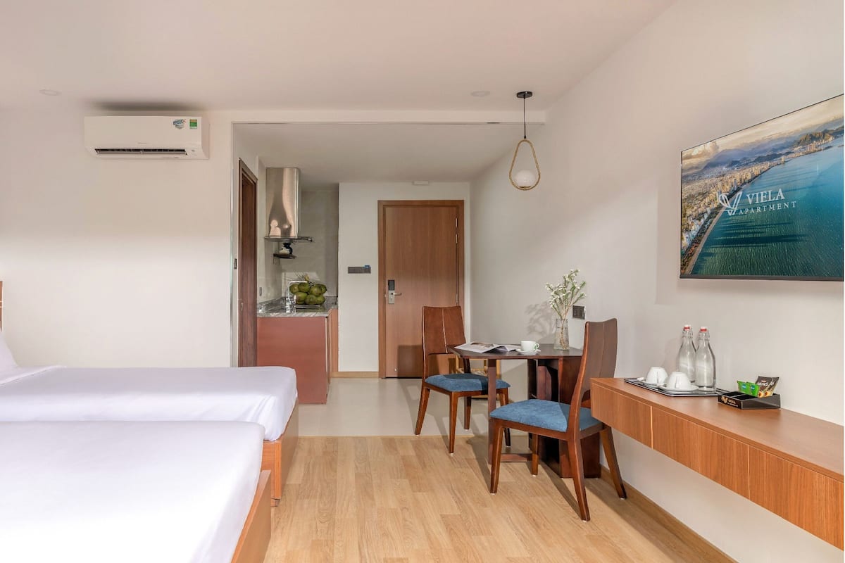 Habitación de hotel con cama, escritorio y sillas, mesa de comedor y un cuadro de una ciudad costera.