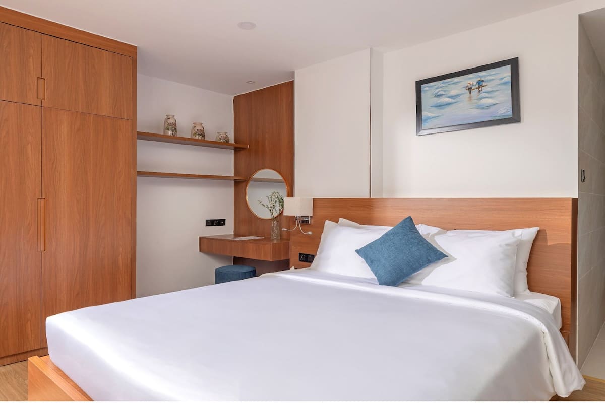 Habitación de hotel con una cama grande, armario de madera, escritorio con espejo y un cuadro en la pared.