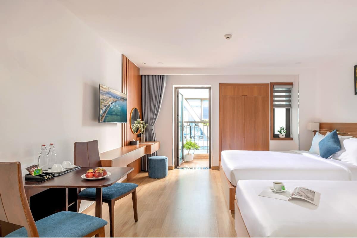 Habitación de hotel con cama, escritorio con silla, televisión y balcón con vistas.