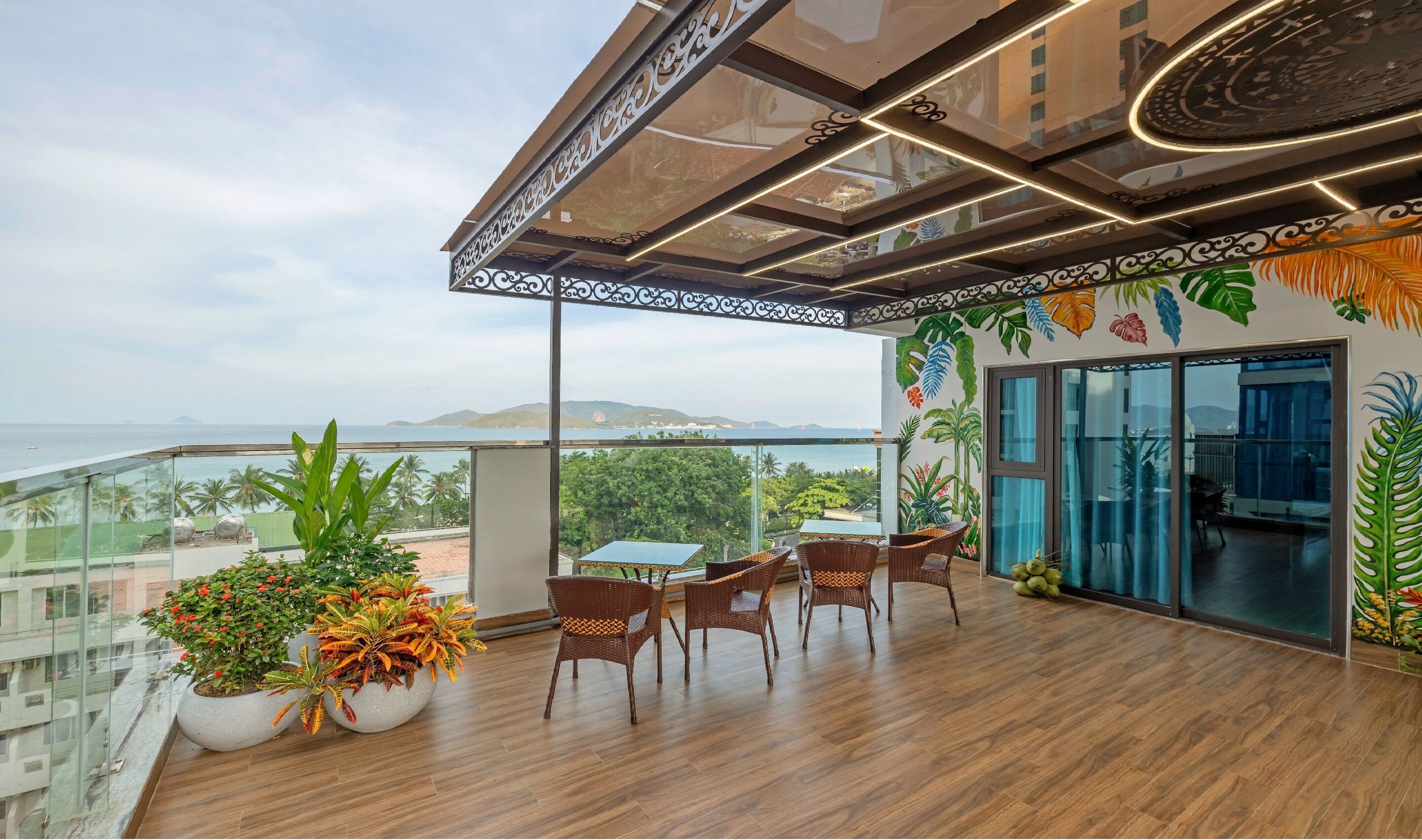 A balcony with wooden flooring, wicker chairs, a table, and potted plants.