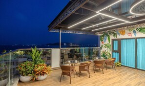 A rooftop terrace with wicker furniture, potted plants, and a view of the sea at night. - Viela Apartment Nha Trang  (Nha Trang)