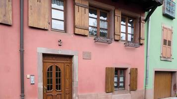 Un bâtiment à la façade rose, avec des volets en bois et une porte portant un numéro.