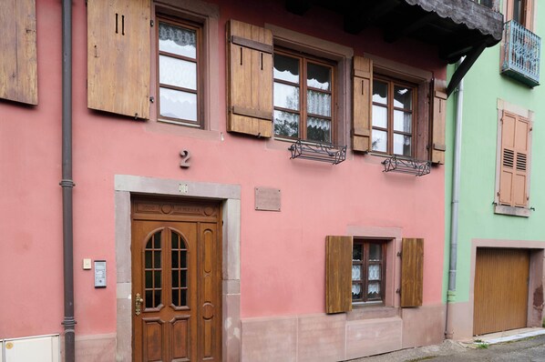 Um edifício com fachada rosa, persianas de madeira e uma porta numerada.