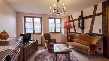 Un salon chaleureux avec un canapé en bois, un téléviseur, un lustre et une grande fenêtre avec des rideaux.