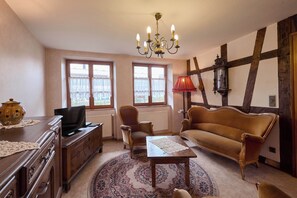 Uma sala de estar aconchegante com um sofá de madeira, uma televisão, um candelabro e uma janela grande com cortinas.