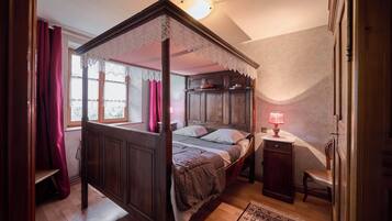 Un lit à baldaquin avec un ciel de lit en dentelle, une tête de lit en bois et une table de chevet avec une lampe.