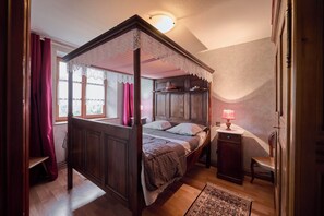 Uma cama de dossel com cortina de renda, cabeceira de madeira e uma mesa de cabeceira com abajur.