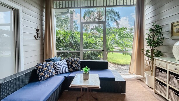 A room with a large window, a sofa with patterned cushions, a small table with a plant, and a cabinet with baskets. - Greenlinks/Lely Condo-1st flr,end unit,Bldg.100/3BR,3BA ensuites/Upscale,Newly Renovated w/lk view (Naples)