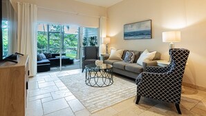 A spacious living room with a large sliding glass door leading to a balcony, a sofa set, a patterned armchair, and a painting on the wall. - Greenlinks/Lely Condo-1st flr,end unit,Bldg.100/3BR,3BA ensuites/Upscale,Newly Renovated w/lk view (Naples)