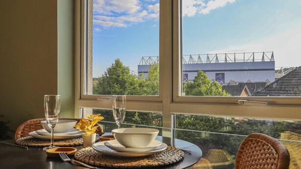 A dining table with a view of a building through a window. - Two-Bedroom Townhouse (Cardiff)