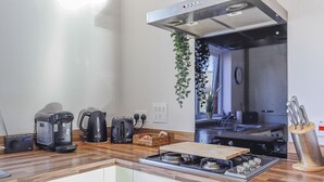 A modern kitchen with a gas stove, coffee maker, toaster, and hanging plants. - Two-Bedroom Townhouse (Cardiff)