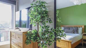 A bedroom with a bed, a dresser, a TV, and a large green plant. - Two-Bedroom Townhouse (Cardiff)