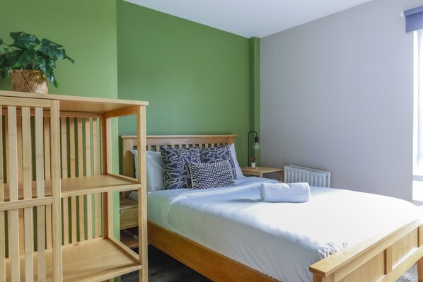 A room with a bed, wooden shelves, a potted plant, and a nightstand with a lamp.
