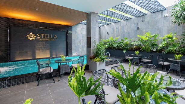 A modern hotel atrium with a swimming pool, outdoor seating, and a prominent "STELLA HOTEL & APARTMENT" sign. - Stella Hotel & Apartment (Ho Chi Minh City)