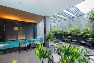 Un moderno vestíbulo de hotel con piscina, asientos exteriores y un llamativo letrero que dice "STELLA HOTEL & APARTMENT".