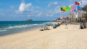 A beach with a row of flags, a sandy shore, and a small island in the distance. - Stella Hotel & Apartment (Ho Chi Minh City)