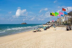 Una playa con una hilera de banderas, una orilla arenosa y una pequeña isla a lo lejos.