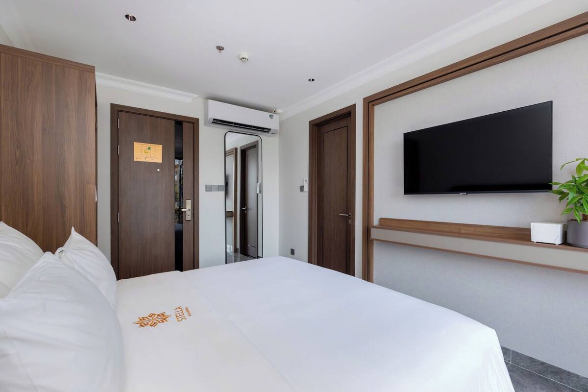 Habitación de hotel con una cama grande, un televisor de pantalla plana en la pared, un armario de madera y un pequeño estante con una planta.