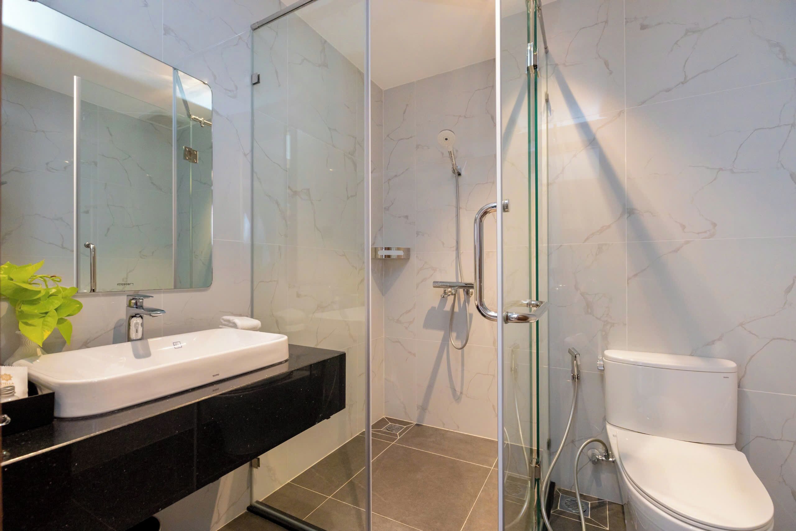 Ein modernes Badezimmer mit einer Glaskabine zur Dusche, einem weißen Waschbecken mit schwarzer Arbeitsplatte und einer weißen Toilette.