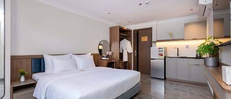 A modern hotel room with a large bed, a small desk, a wardrobe, a kitchenette, and a bathroom.