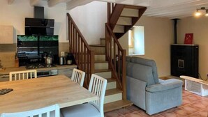 A compact kitchen with a wooden staircase, a dining table with chairs, and a grey armchair. - Gîte du Cady (Casteil)