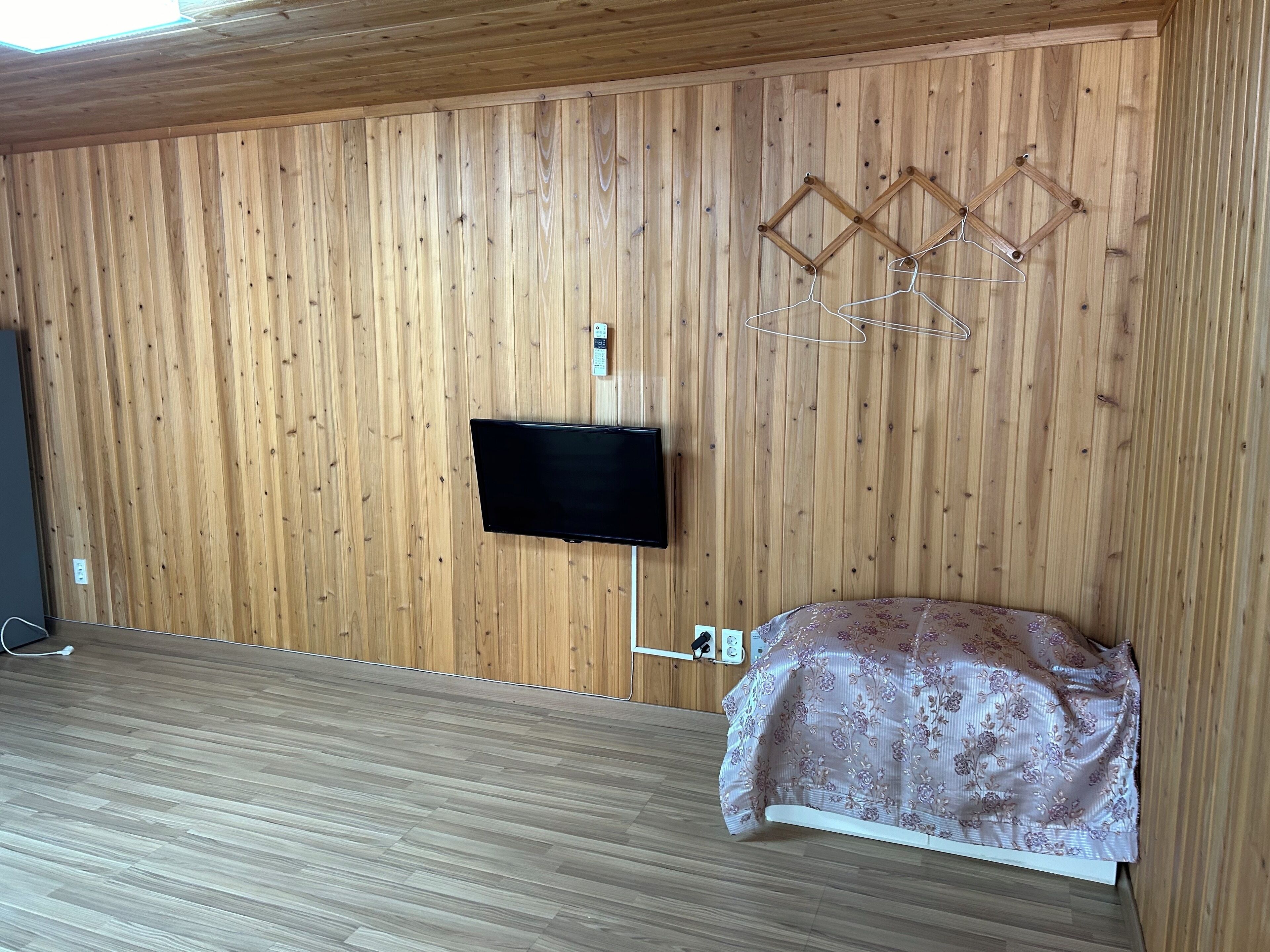 Een kamer met een houten lambrisering, een tv aan de muur en een bed met een bloemenprint deken.