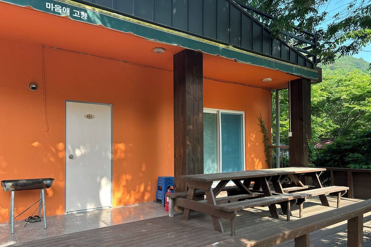 A wooden deck with picnic tables, a door, and a small trash bin.