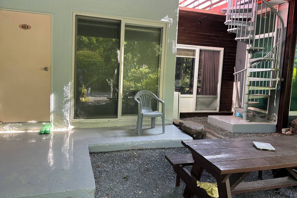 A room with a sliding glass door, a wooden staircase, a plastic chair, and a picnic table.