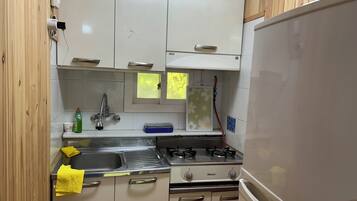 A compact kitchen with white cabinets, a stainless steel sink, a gas stove, and a white refrigerator.