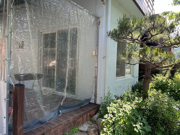 A room with a large window covered by a clear plastic sheet, a wooden bench outside, and a pine tree in the garden. - MAUMAEGOHYANG Pension (Cheongdo)