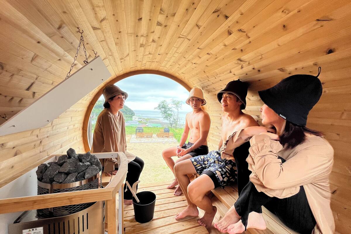 A wooden sauna with a circular opening, wooden benches, and a bucket of stones.