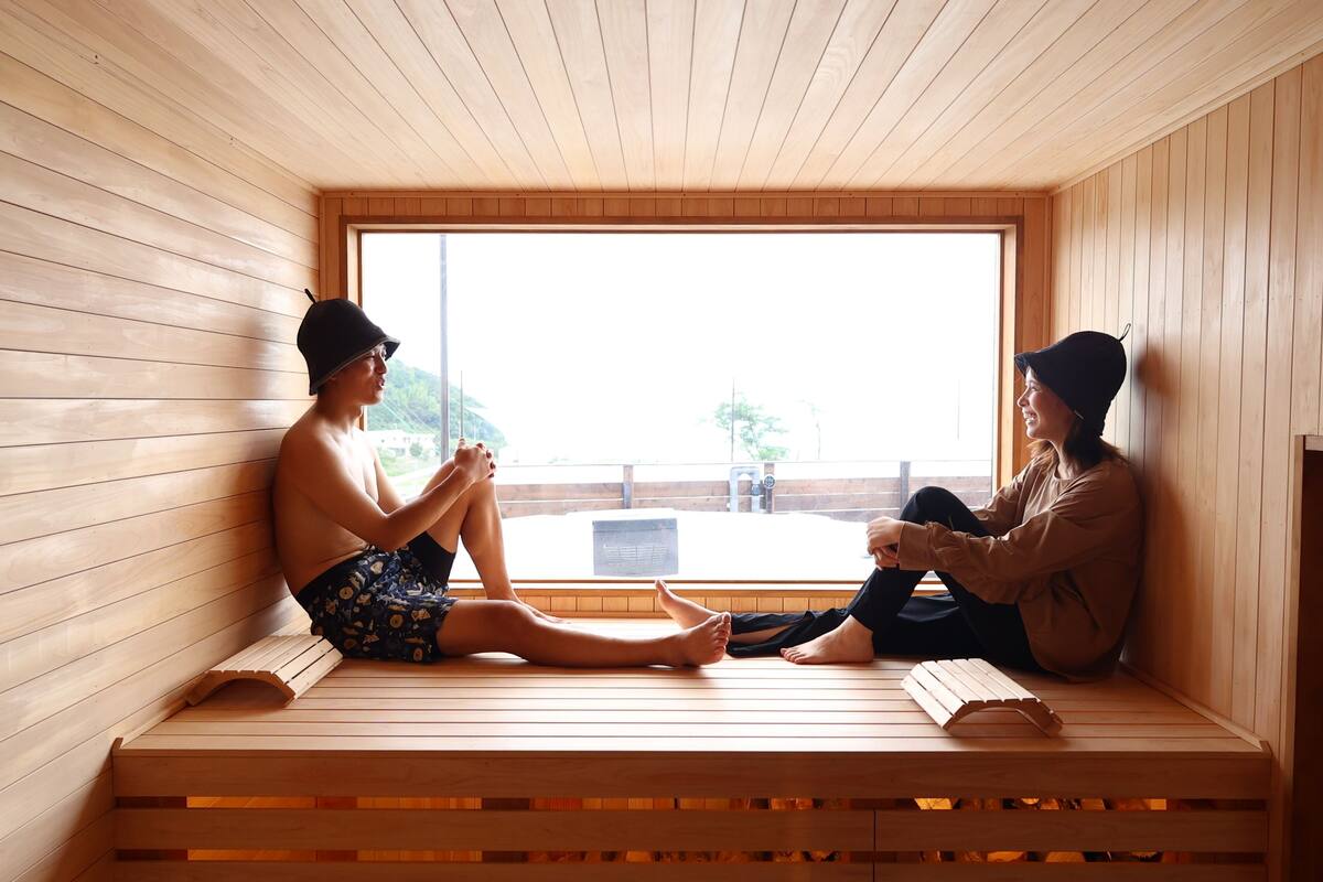 Two people sitting on wooden benches in a sauna room with a large window.