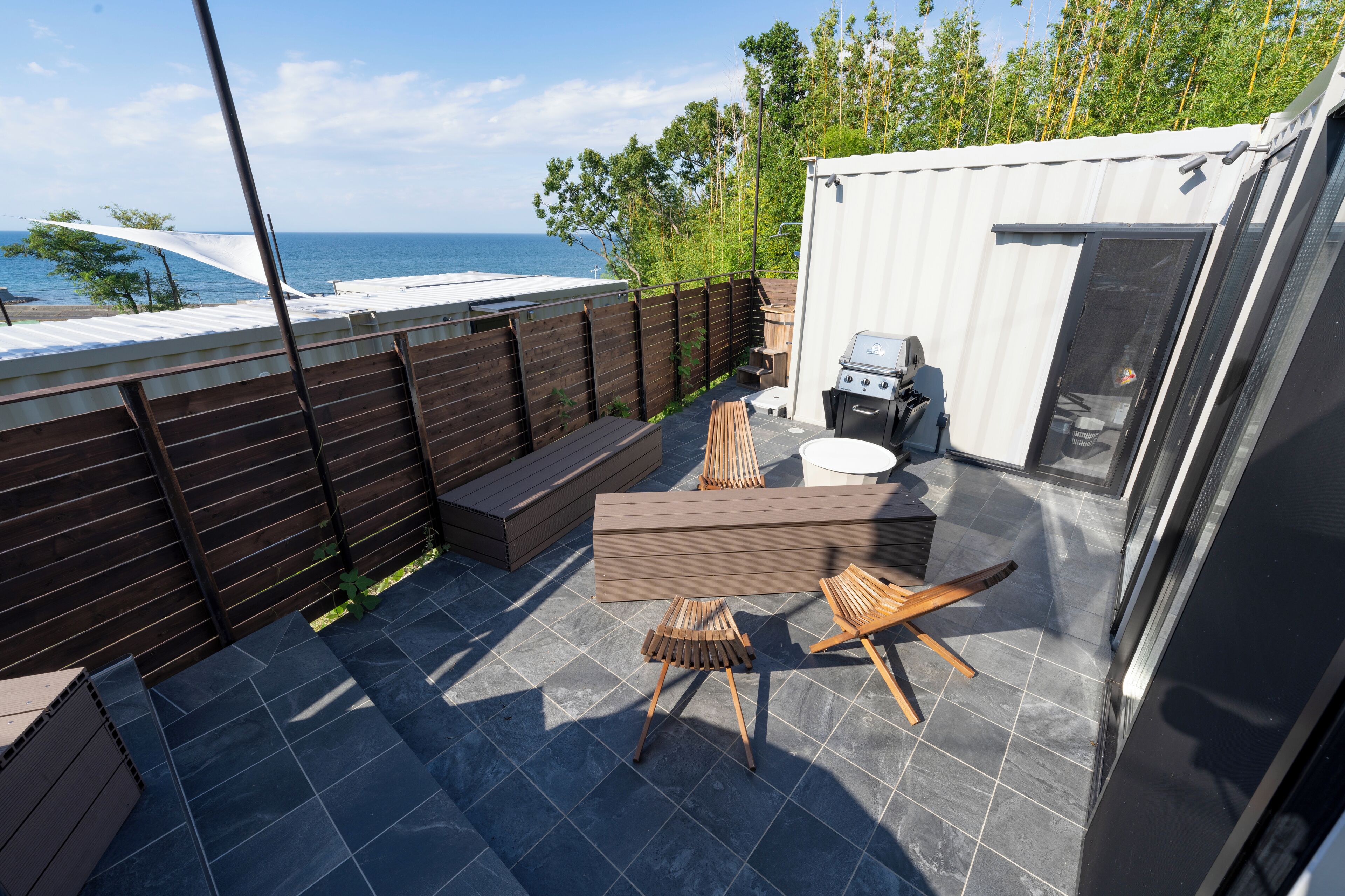 A patio with a view of the sea, a barbecue grill, and outdoor seating.