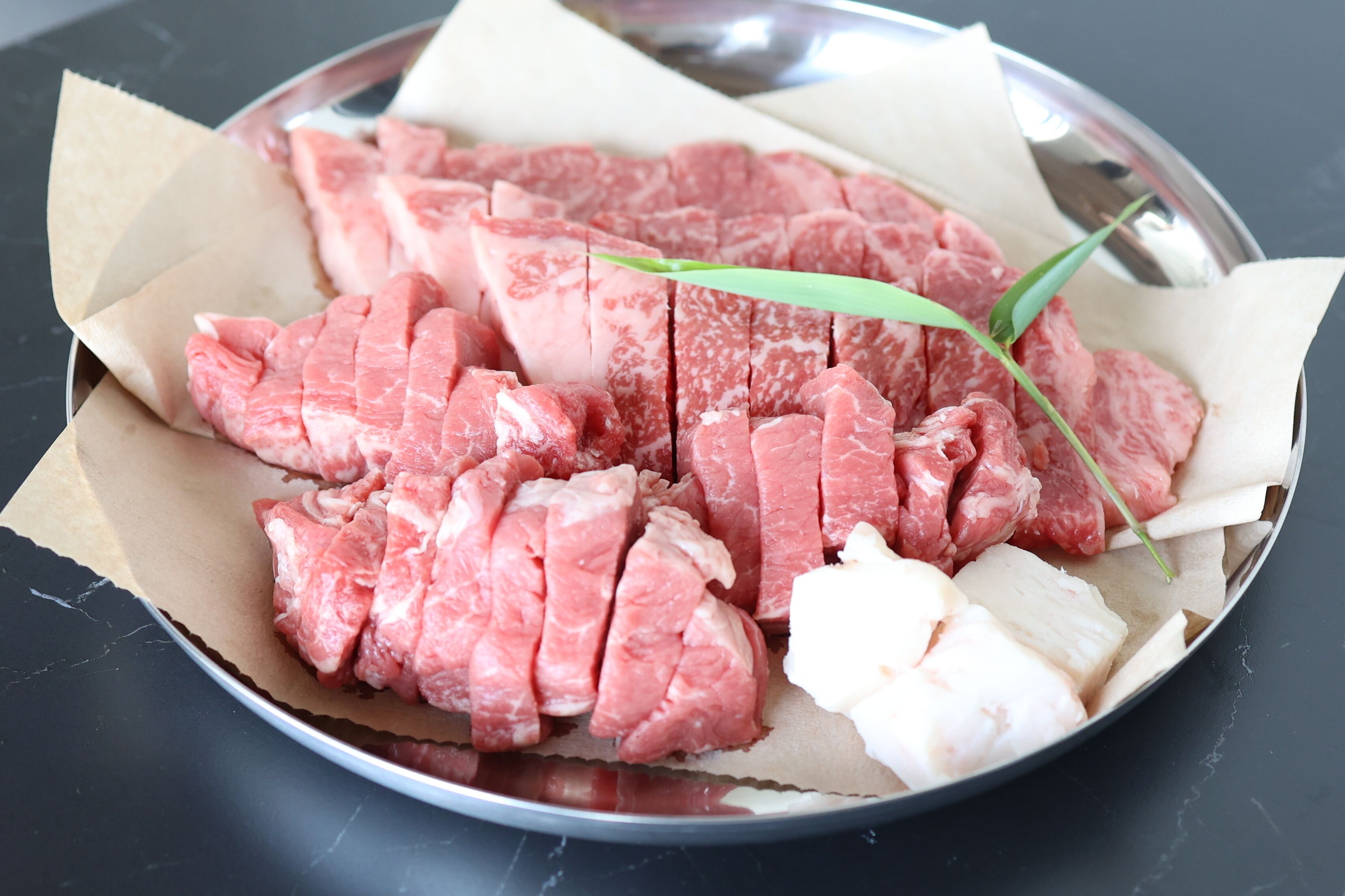 A plate with raw meat and a green leaf on a metal surface.