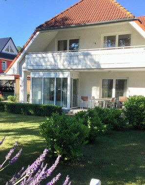 A two-story house with a covered patio, a lawn, and lavender plants. - Gemütliches Apartment 5 mit Abendsonne (Prerow)