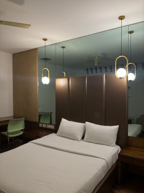 A hotel room with a bed, a desk, and a chair. There are pendant lights above the bed. - Purple Inn (Mysore)