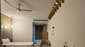 Una habitación de hotel con dos camas individuales, un escritorio con silla, un ventilador de techo y una mesita con un atrezo de artículos de aseo.