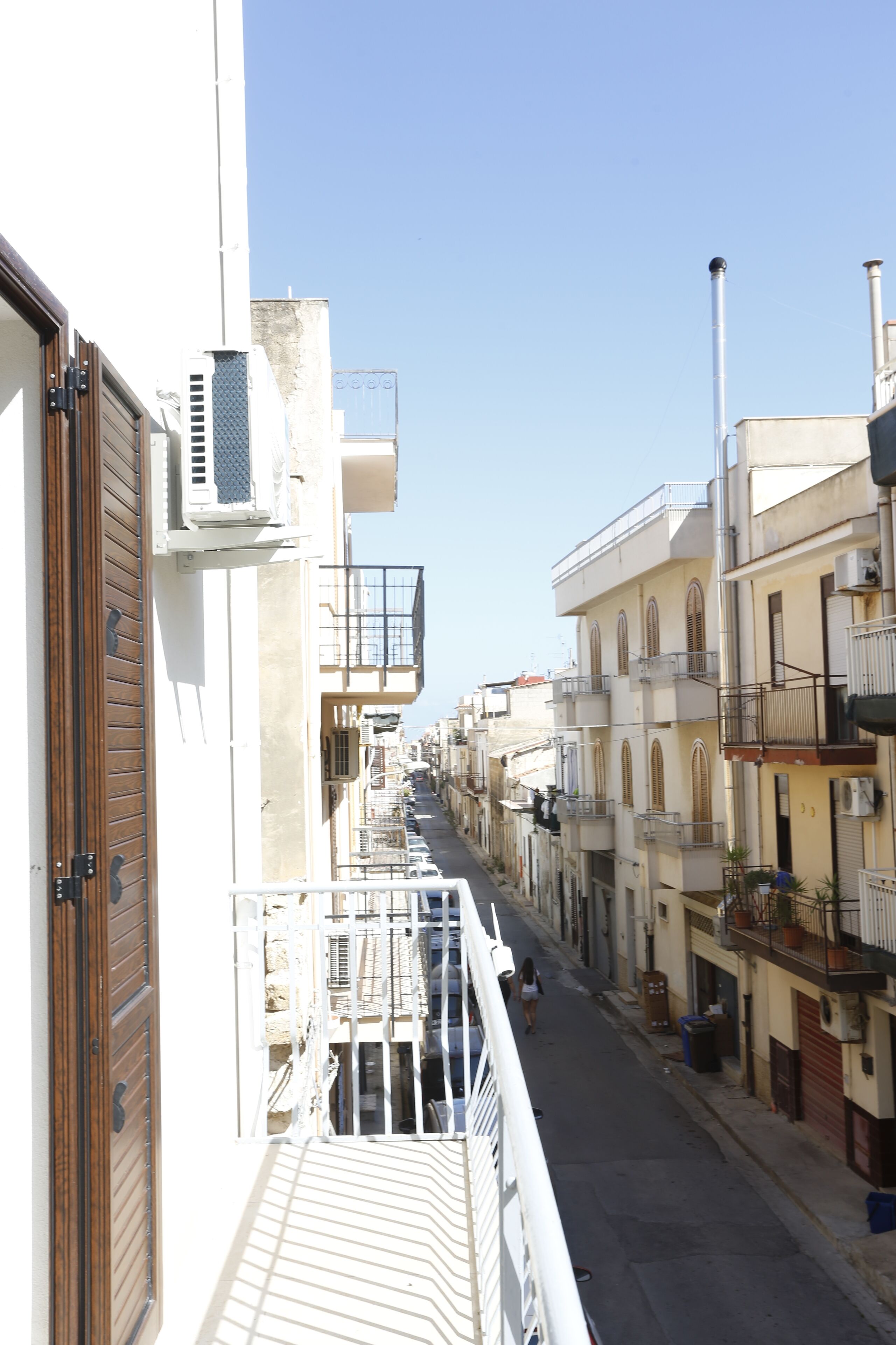 Una stretta via fiancheggiata da edifici, con balconi e cielo sereno.