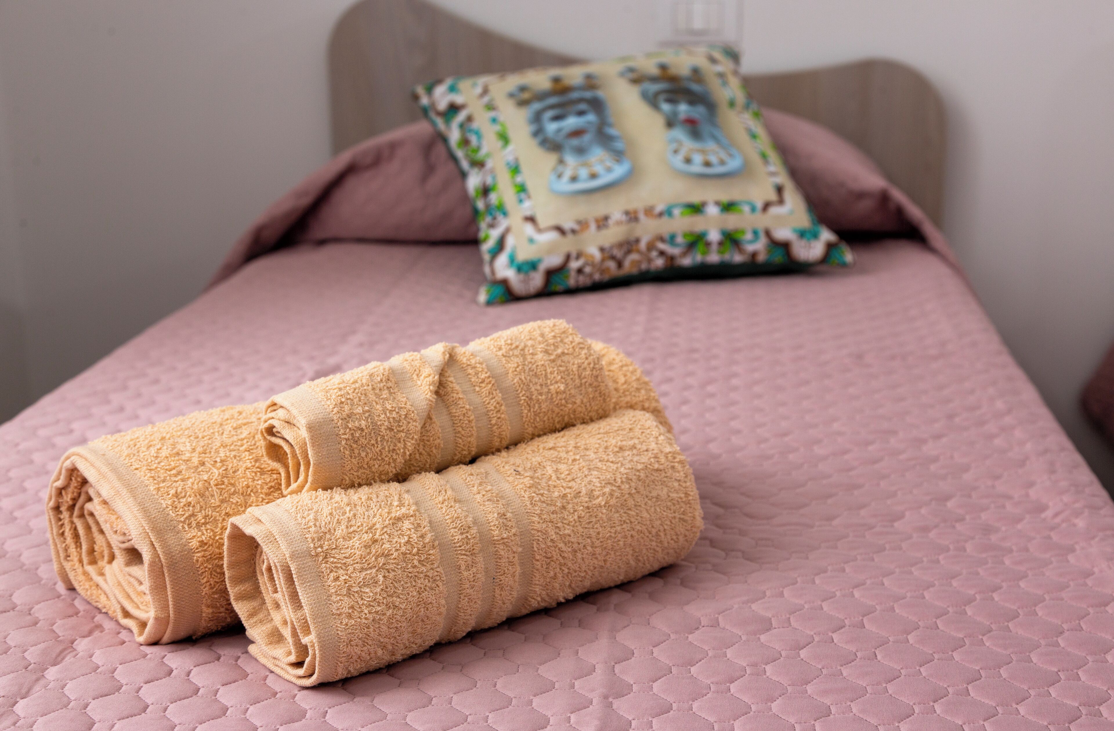 Ein ordentlich bezogenes Bett mit rosa Bettwäsche und zwei aufgerollten Handtüchern.