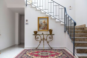 Un escalier avec une rampe noire, un panneau fixé au mur indiquant les numéros des chambres, une table décorative avec deux vases et un tapis à motifs.